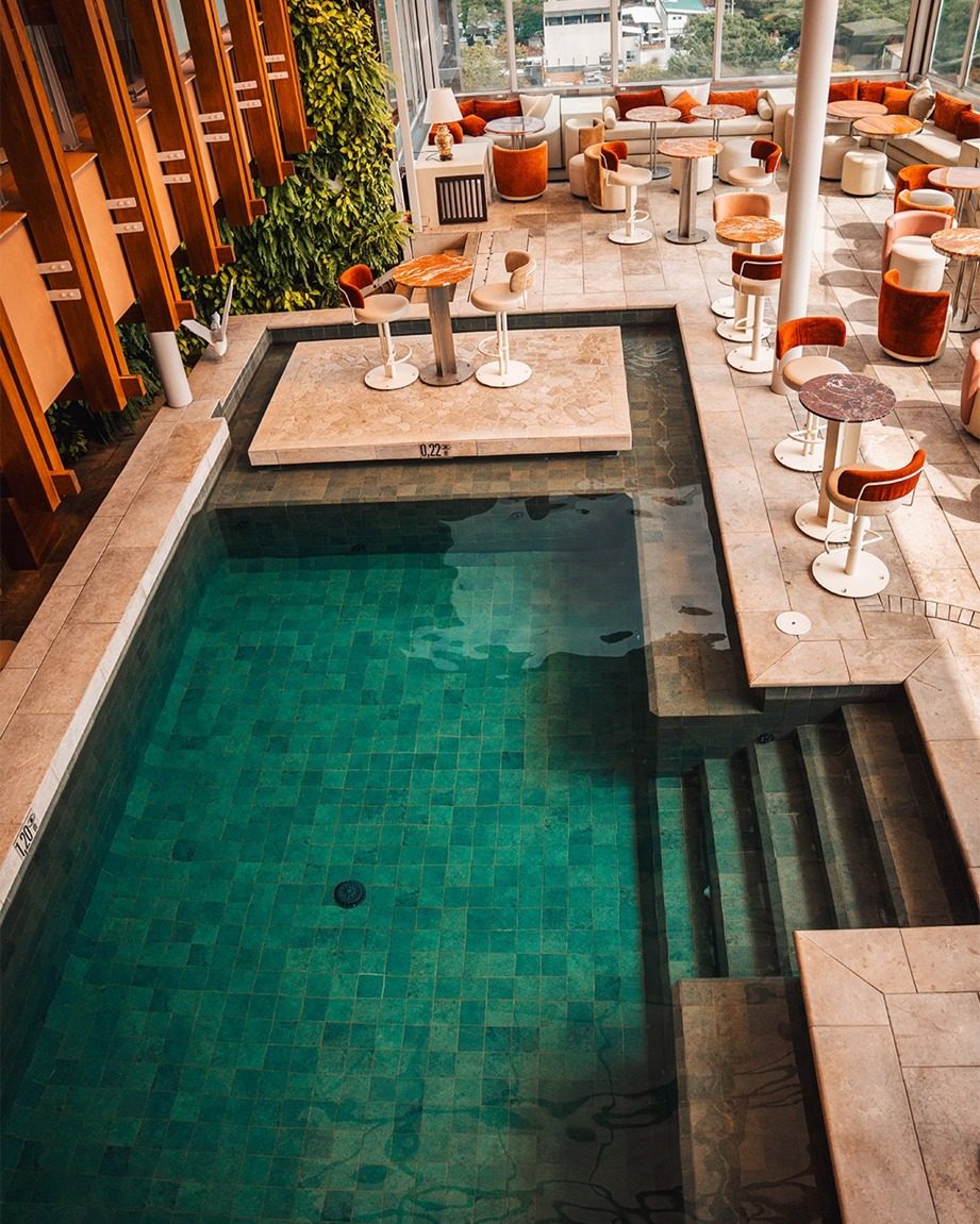 Piscine aux parois de verre et tables sur l'Envy Rooftop